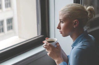 En ansatt med en kaffekopp som ser ut av vinduet.