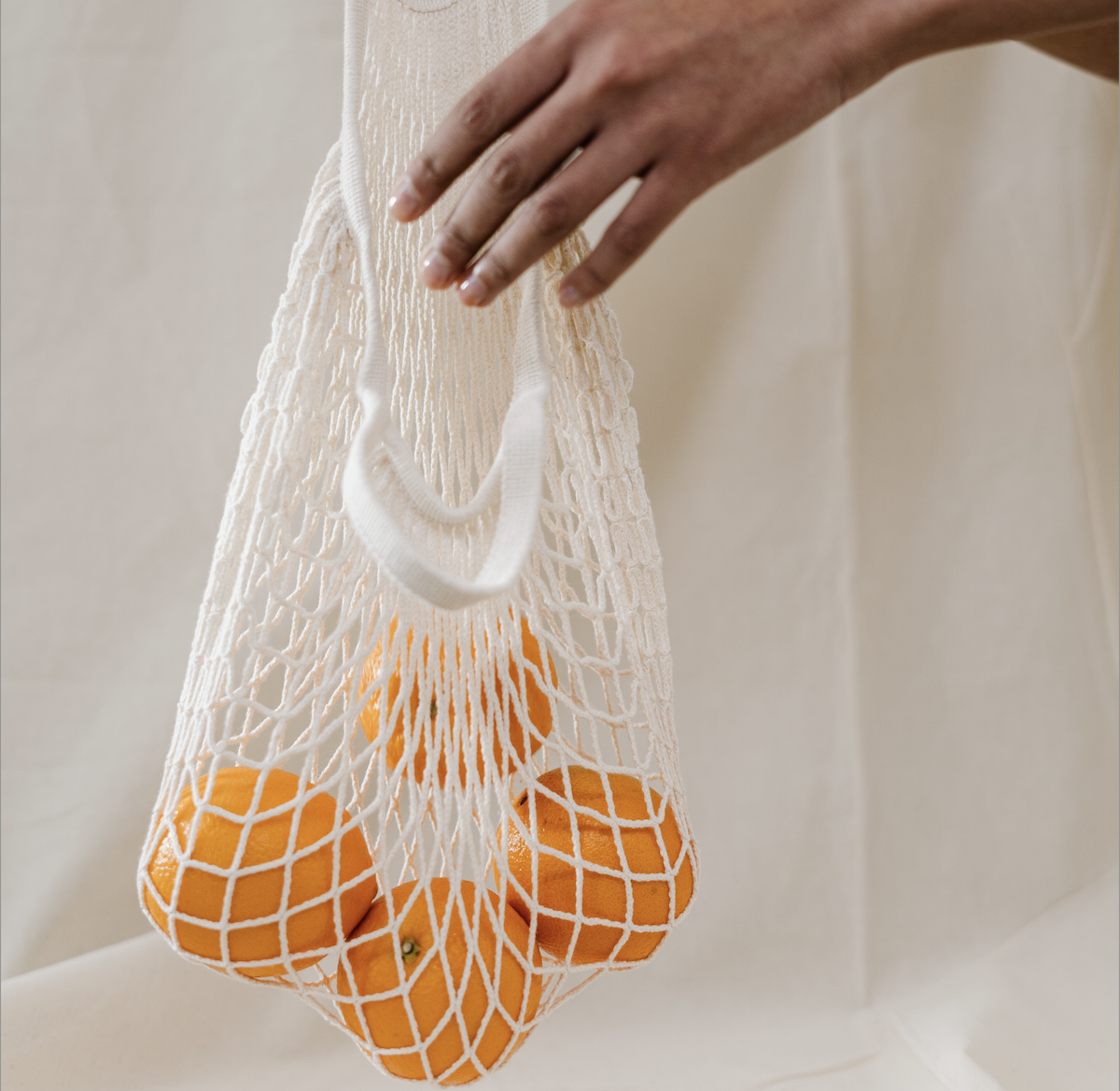 En hånd legger en appelsin ned i et nett med flere appelsiner | Vi jobber for mer bærekraftig mat | Coor