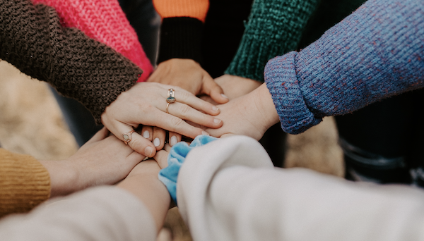 En gruppe mennesker legger hendene sine oppå hverandre | Godt samhold er en del av sosialt ansvar | Coor