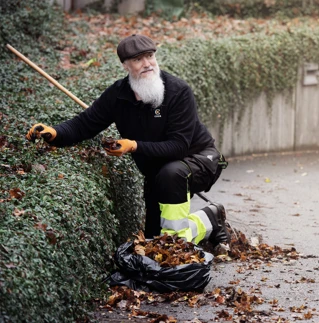 En mann som rydder i bedd og raker løv