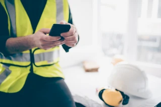 Person i gul vest som ser på mobilen og en hjelm ved siden av