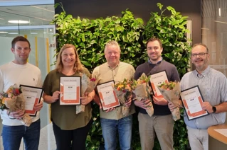 Fem personer som står på rekke og holder opp et innrammet diplom hver