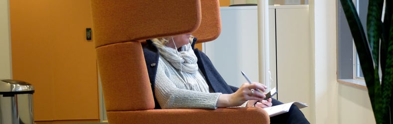En person sitter i en stol og skriver i en notatblokk | Kontorløsninger som gir arbeidsro | Coor 